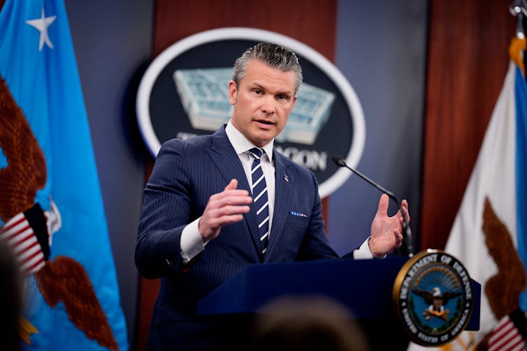 A man in a suit and tie speaks in front of a lecturn.