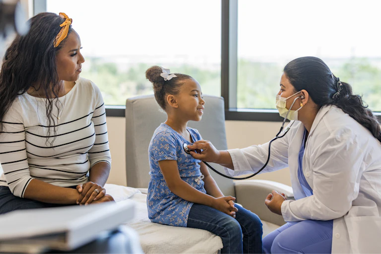 A doctor talks with a young patient while the patient's guardian looks on.