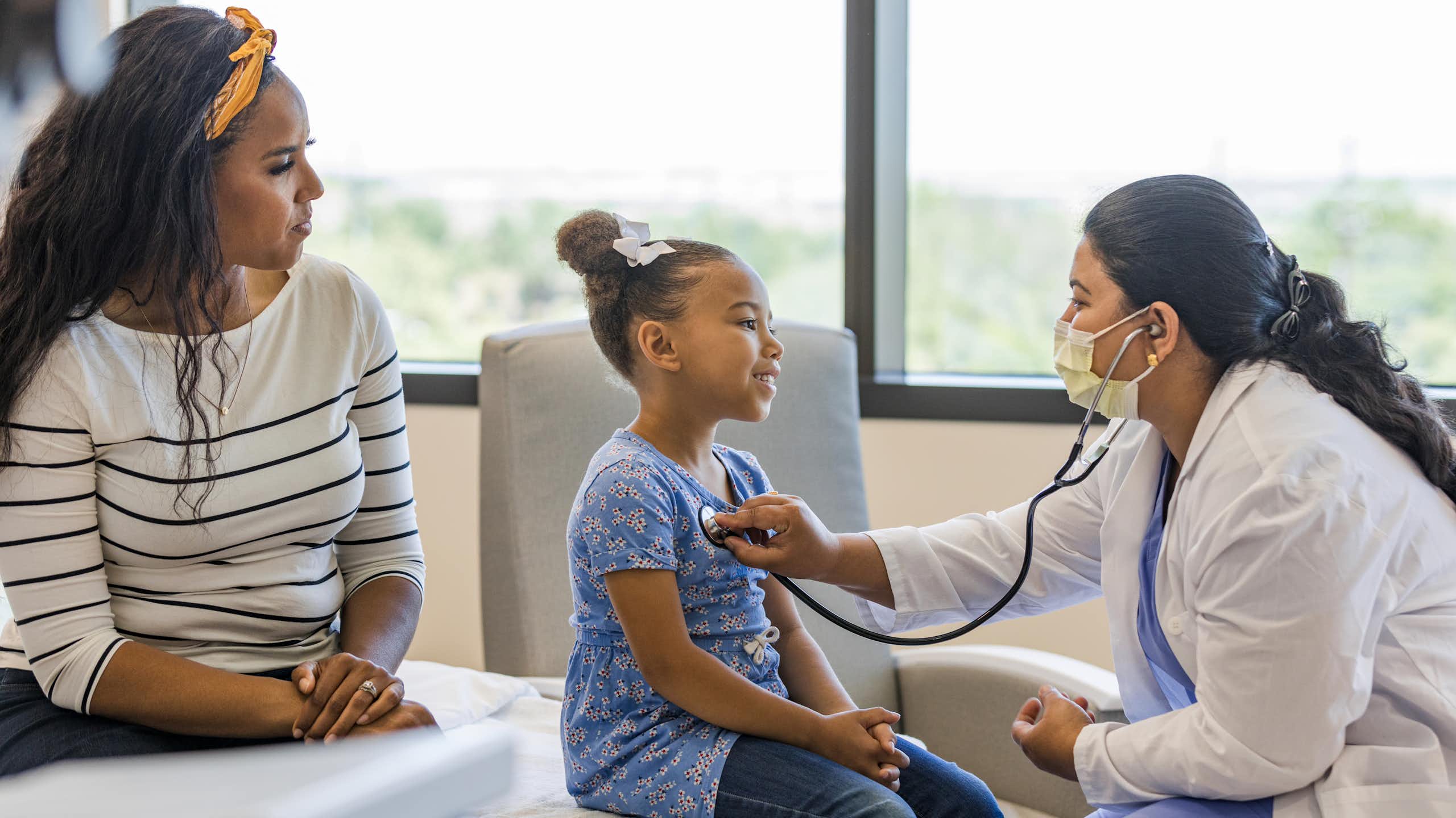 A doctor talks with a young patient while the patient's guardian looks on.