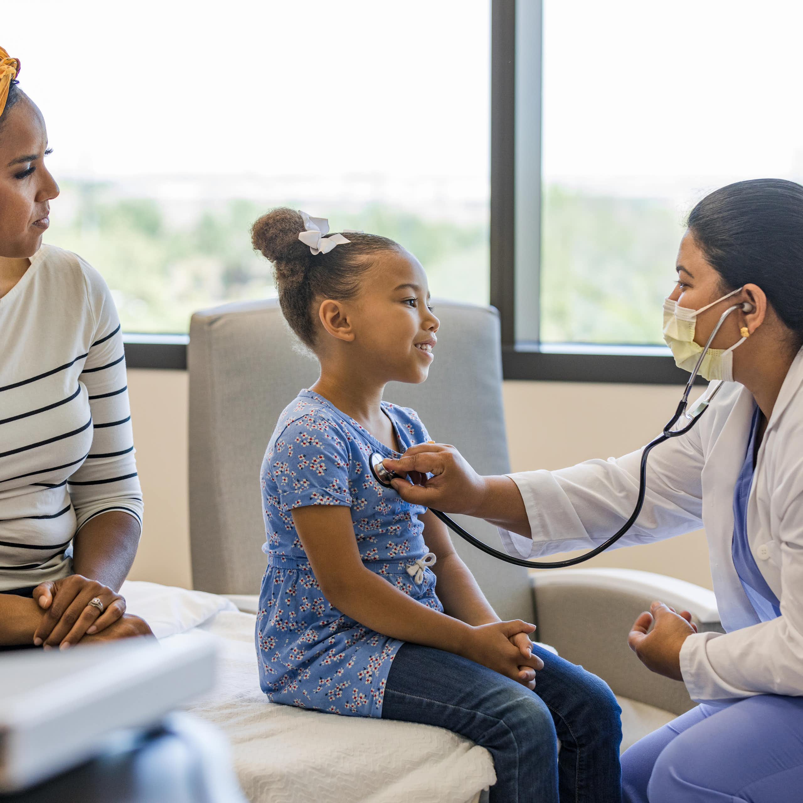 A doctor talks with a young patient while the patient's guardian looks on.