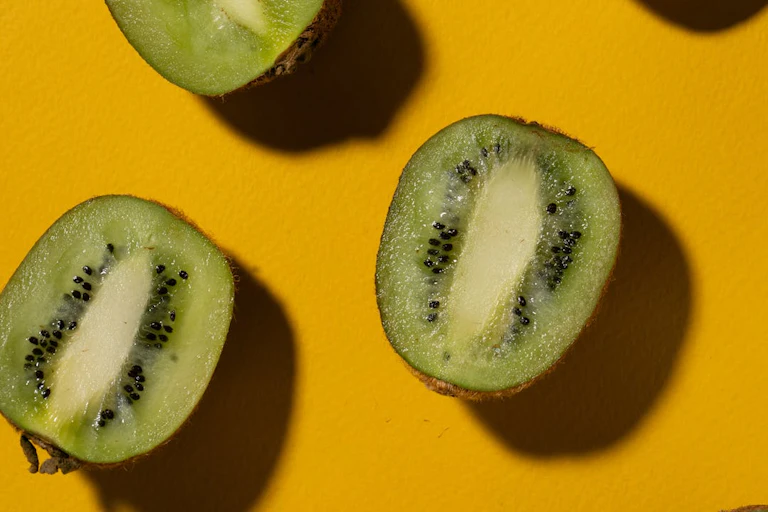 Kiwifruit cut in half lengthwise, arranged diagonally on yellow background