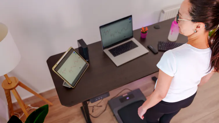 A middle aged white woman walking on a treadmill under a standing desk