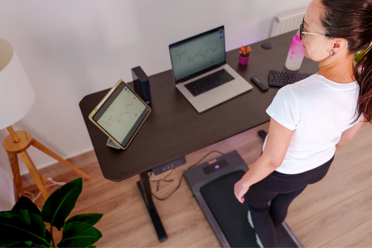 A middle aged white woman walking on a treadmill under a standing desk