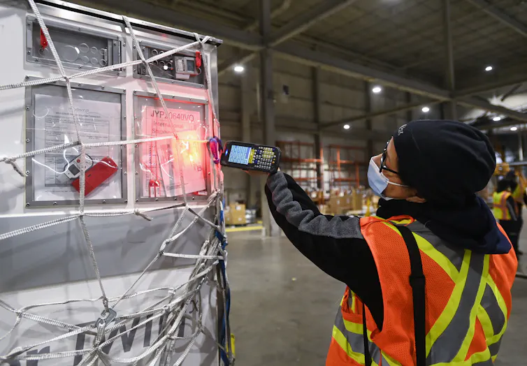 A person in a fluorescent vest scans a giant crate with a handheld scanner