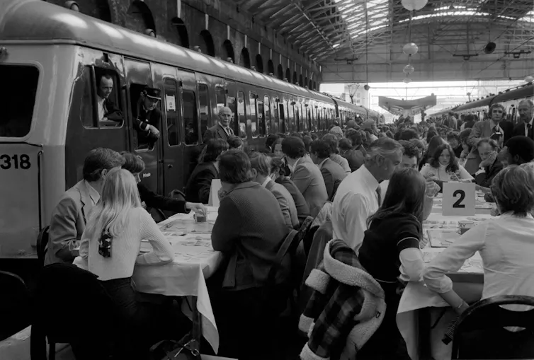 People at tables on train platforms.