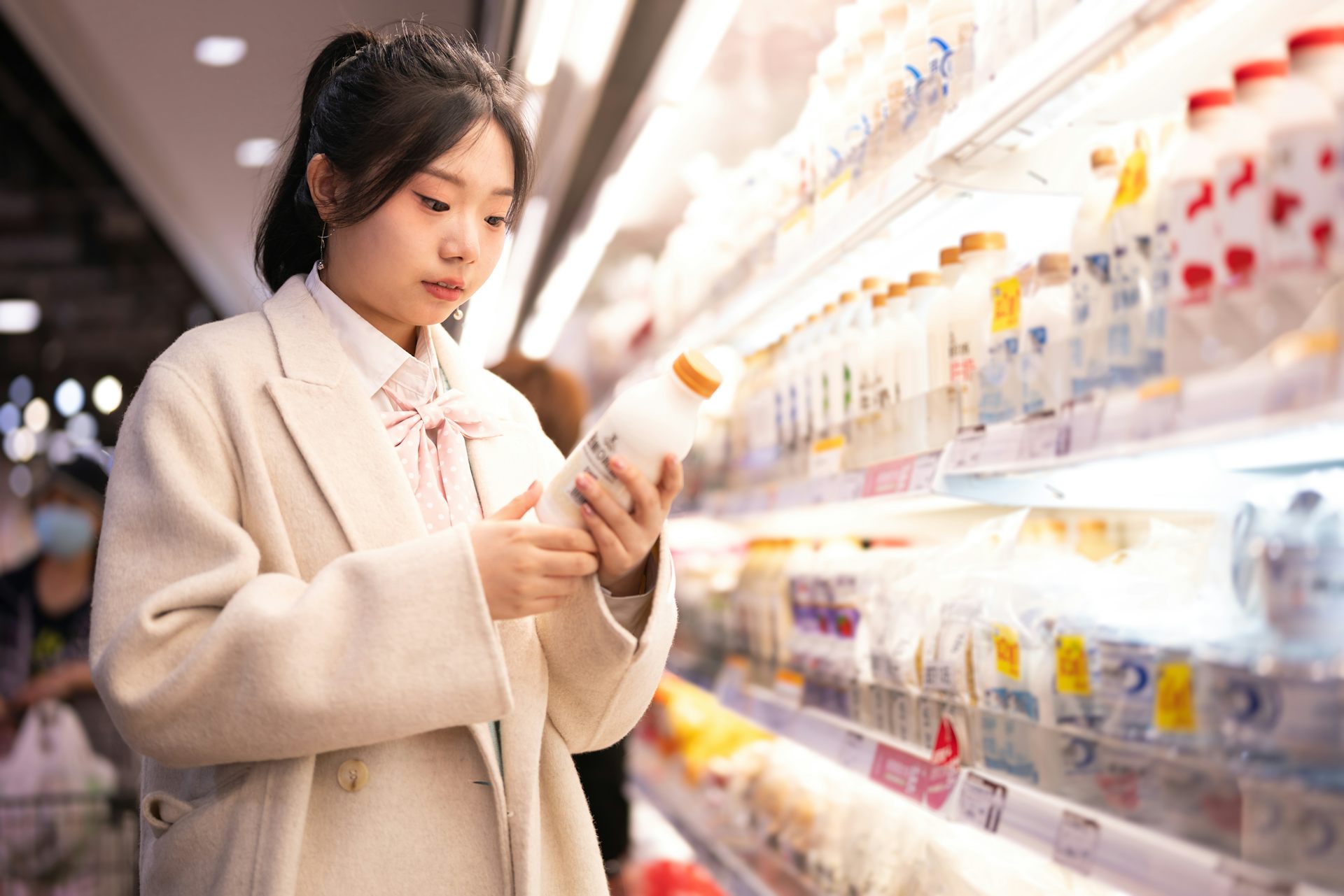 Woman inspects a milk bottle label in a supermarket.