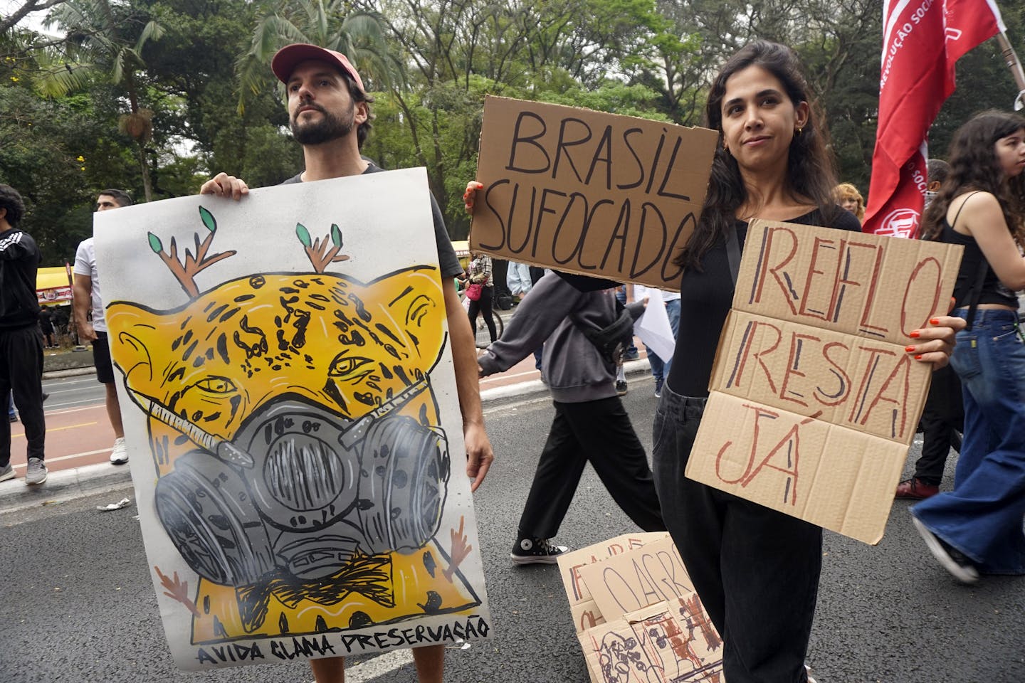 A man and woman hold cardboard signs with words and images protesting the burning of the Amazon forest.