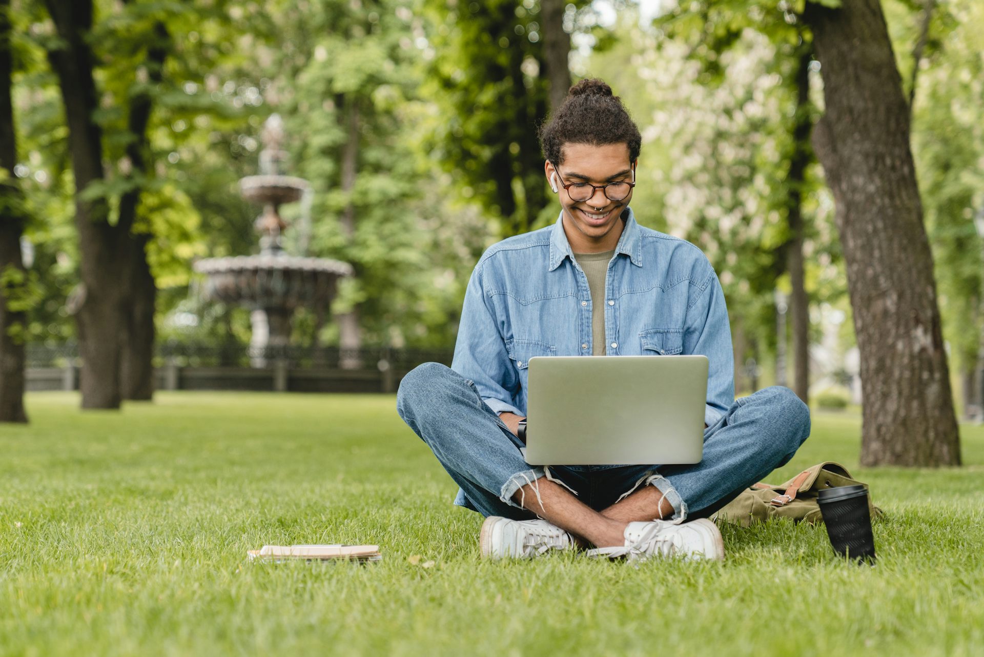 young man sitting with a laptop amid greenery in a park.
