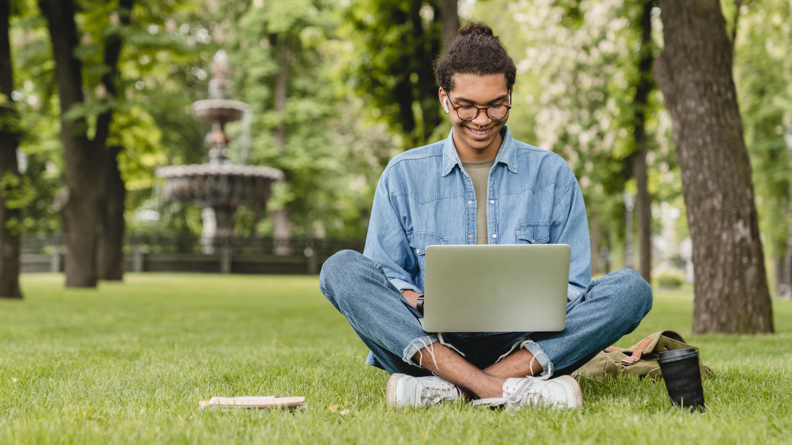 young man sitting with a laptop amid greenery in a park.