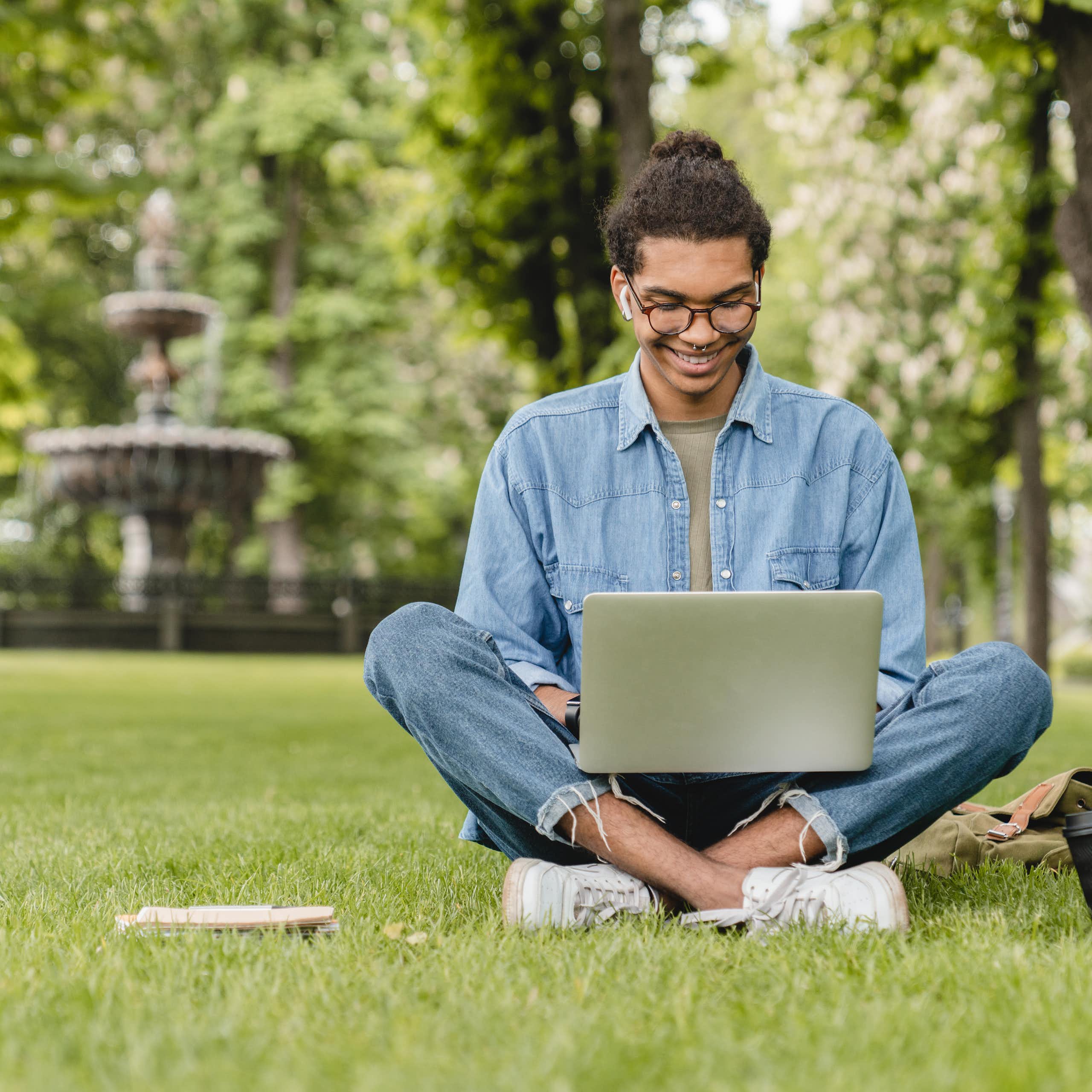young man sitting with a laptop amid greenery in a park.