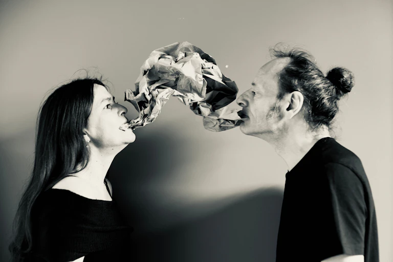 Two people sharing one voice, made visual using crumpled paper flowing between their mouths