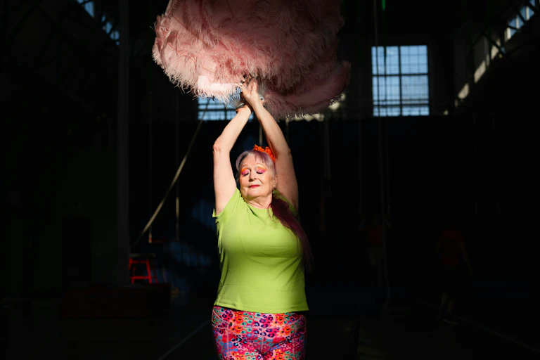 Une femme d’un certain âge agitant des plumes d’autruche roses au-dessus de sa tête, les yeux fermés