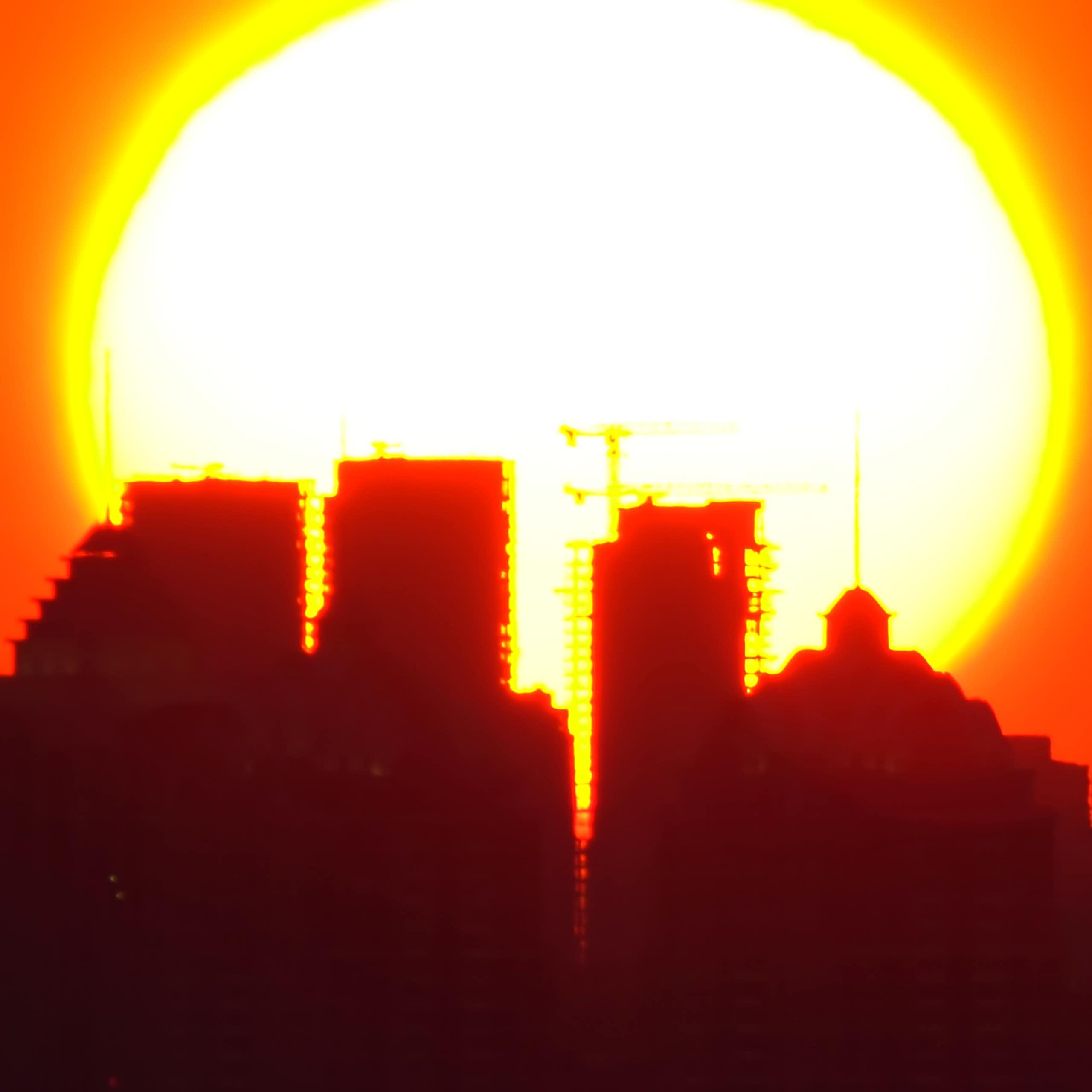 A silhouette of a city with a huge burning sun in an orange sky