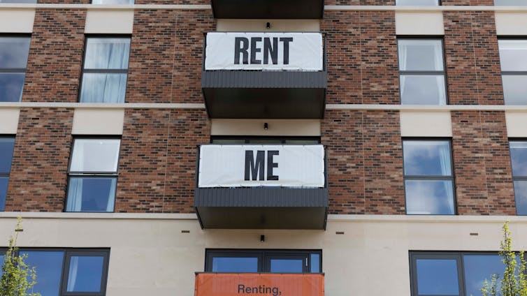 exterior shot of a block of flats with banners reading 'rent me' draped from the balconies.