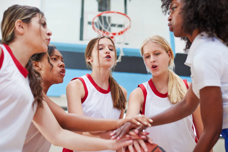Jóvenes jugadoras de baloncesto juntan sus manos para darse ánimo.