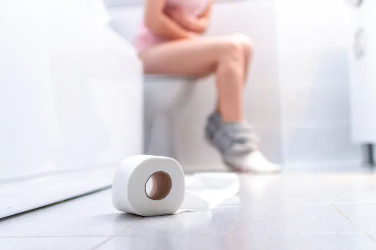 Woman sitting on a toilet, holding her stomach in agony.