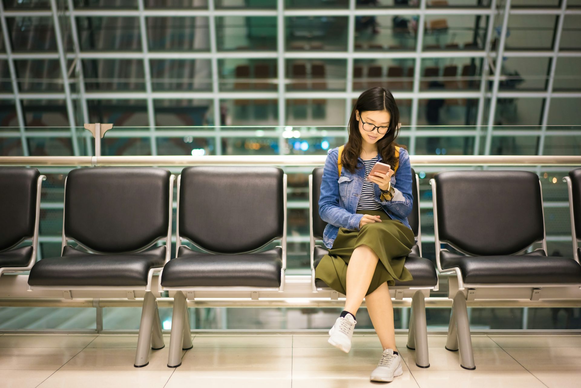 A young woman sitting at an airport, looking at her mobile phone