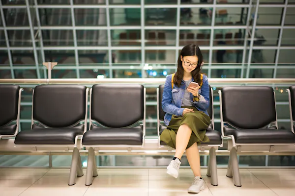A young woman sitting at an airport, looking at her mobile phone