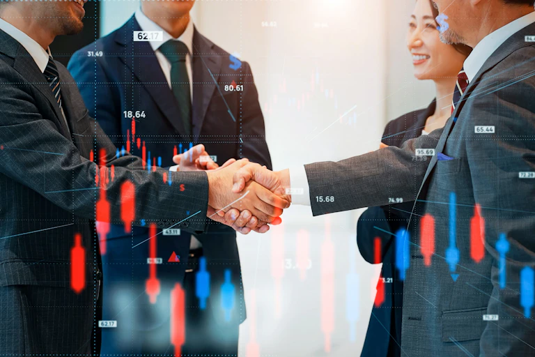 Personnes en costume se serrant la main devant des graphiques financiers.
