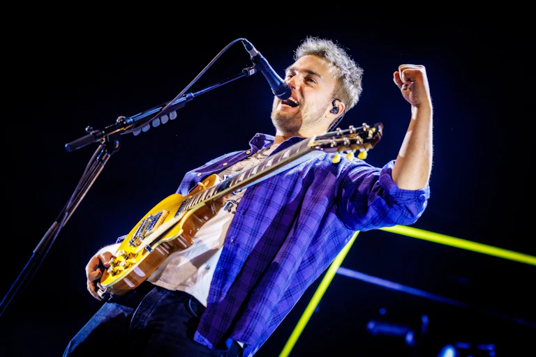 A young white guy on stage with his guitar his fist raised aloft.