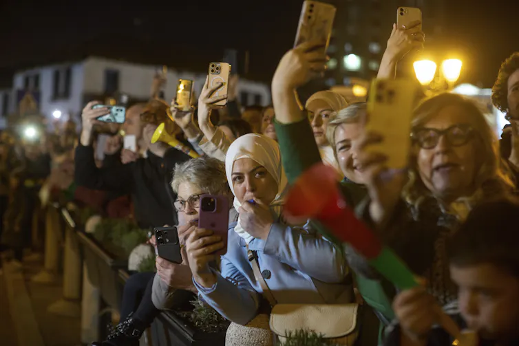 Camera-wielding people wait expectantly behind a line for the arrival of others.