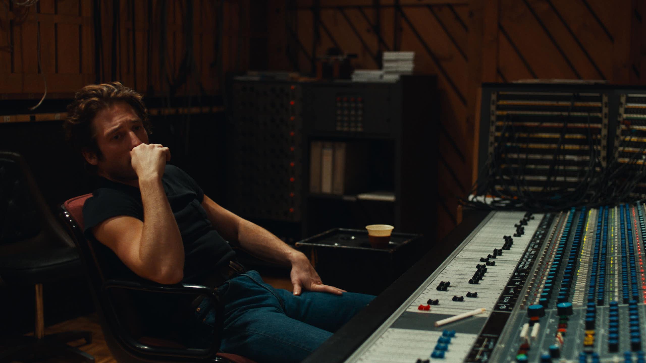 Un hombre joven en vaqueros está sentado pensando en un estudio de grabación.