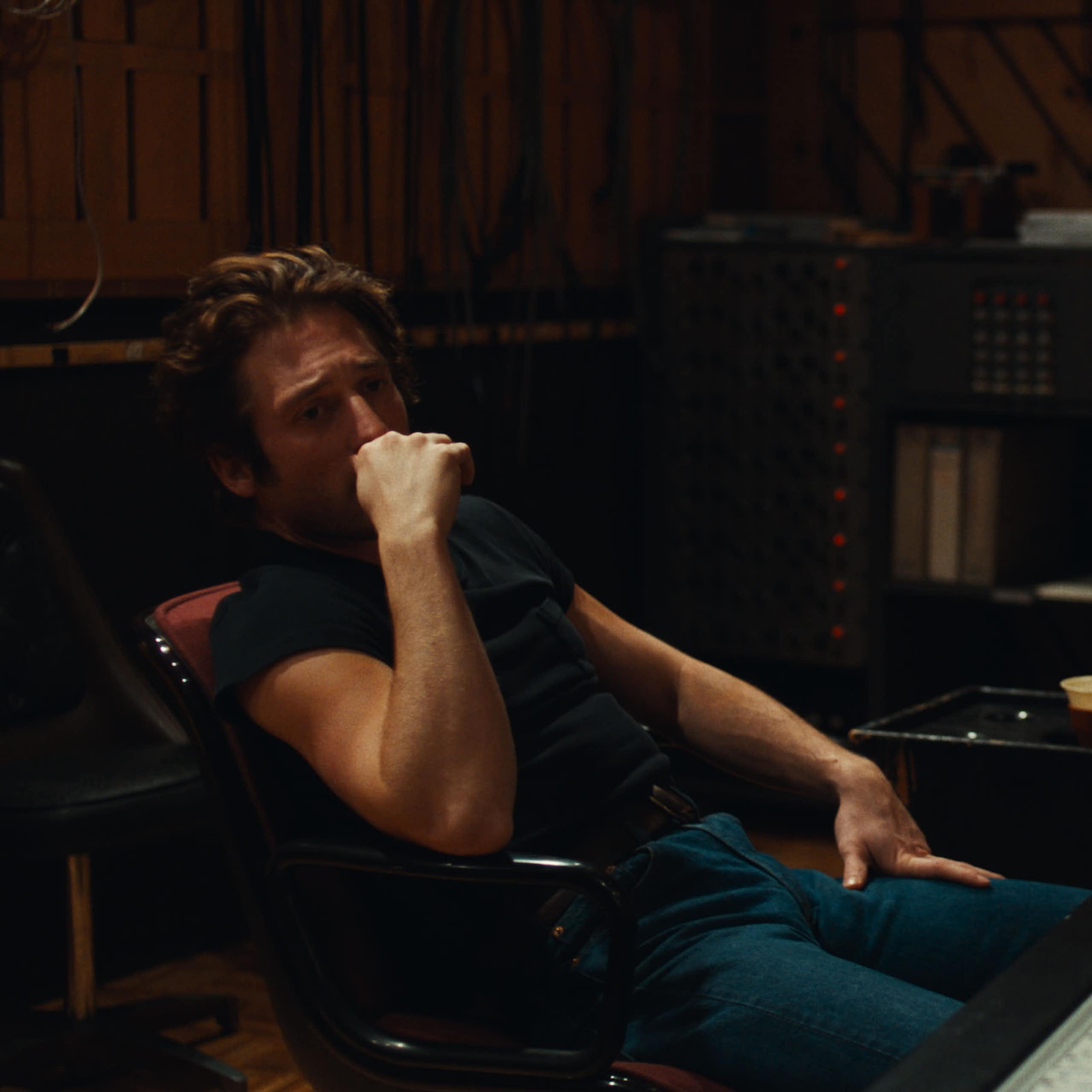 Un hombre joven en vaqueros está sentado pensando en un estudio de grabación.