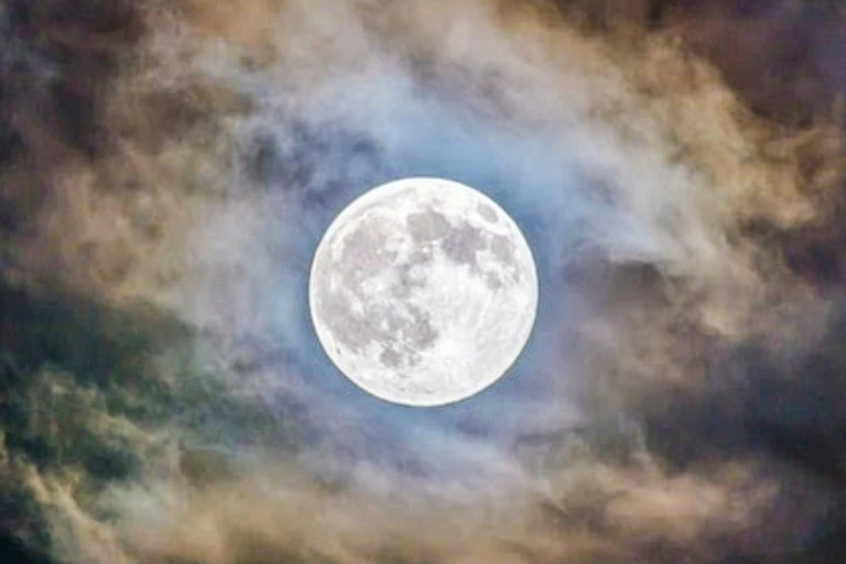 Large, bright full moon high in the sky, shrouded by eery-looking clouds.