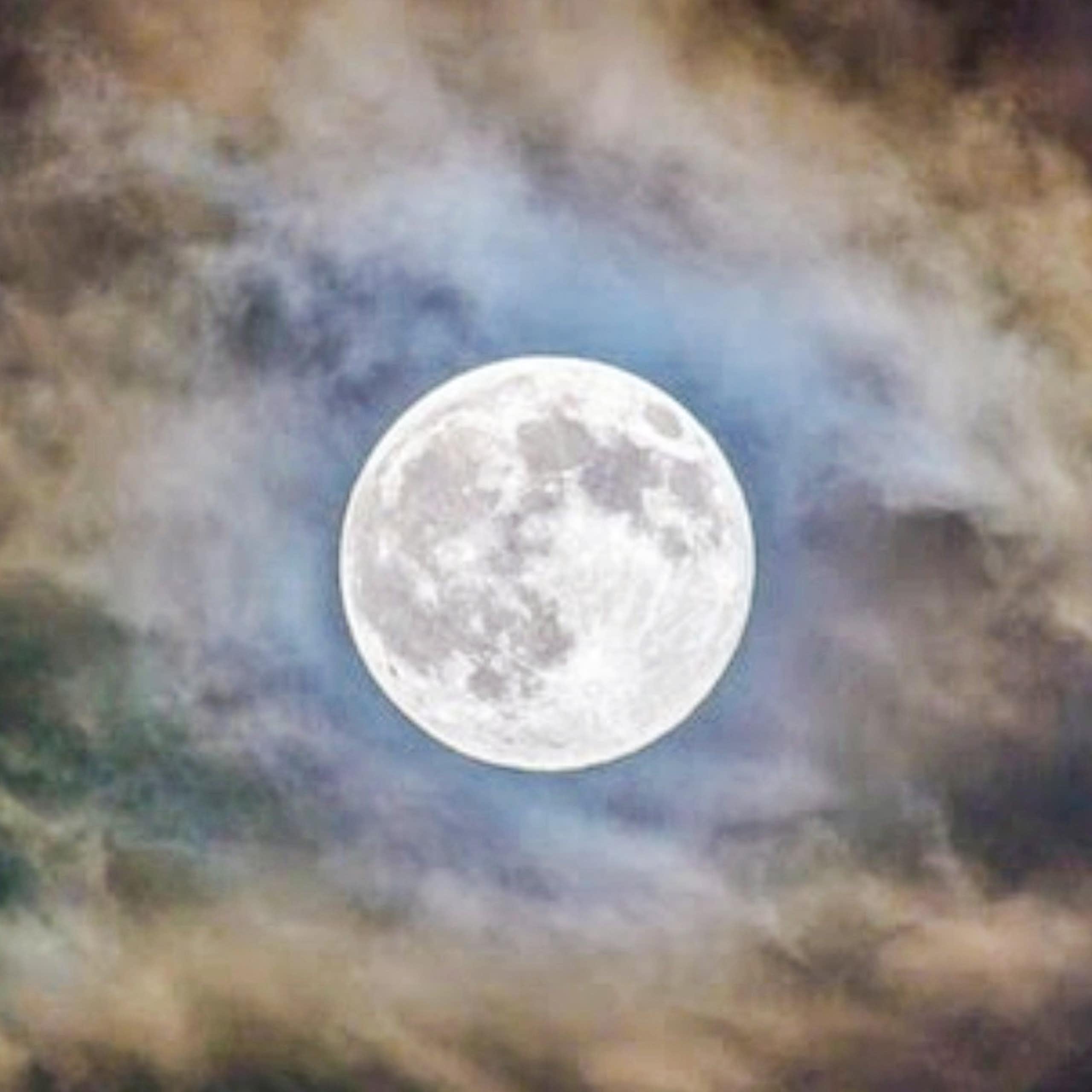 Large, bright full moon high in the sky, shrouded by eery-looking clouds.