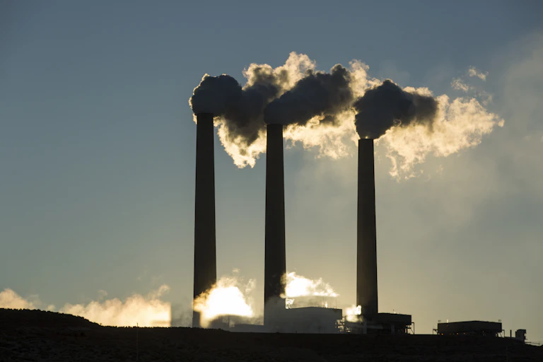 Three tall smokestacks emit smoke and steam into the atmosphere.