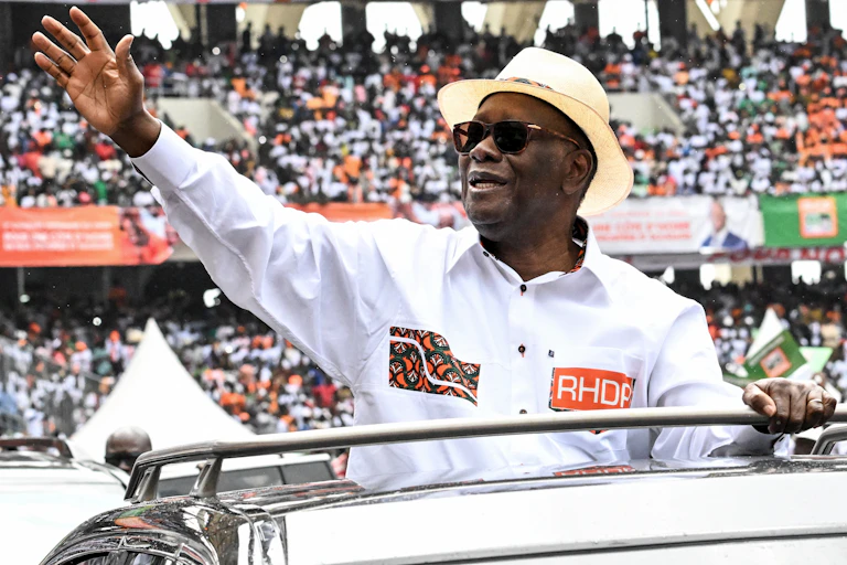 Man wearing a white shirt and bowler hat, waving at a large crowd