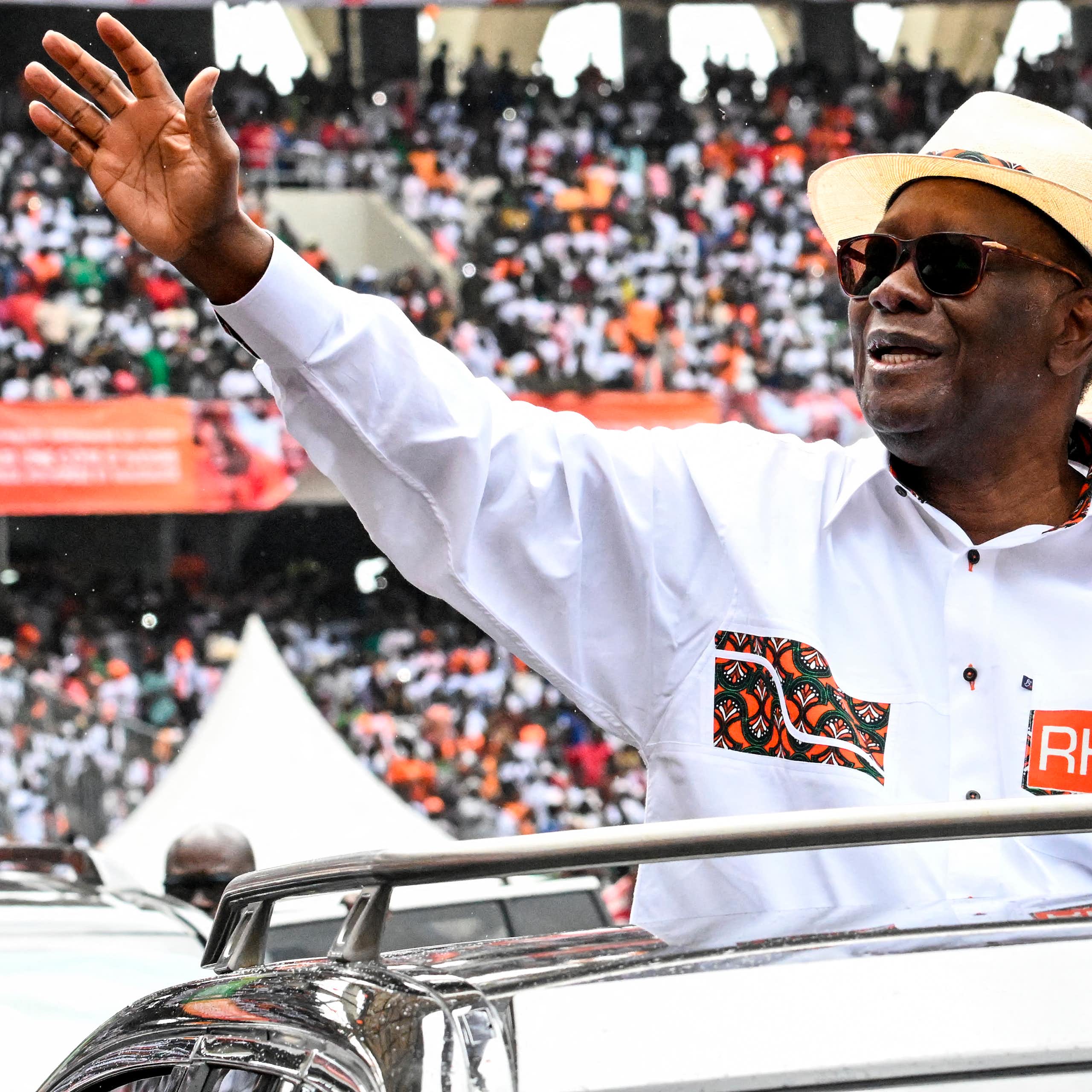 Man wearing a white shirt and bowler hat, waving at a large crowd