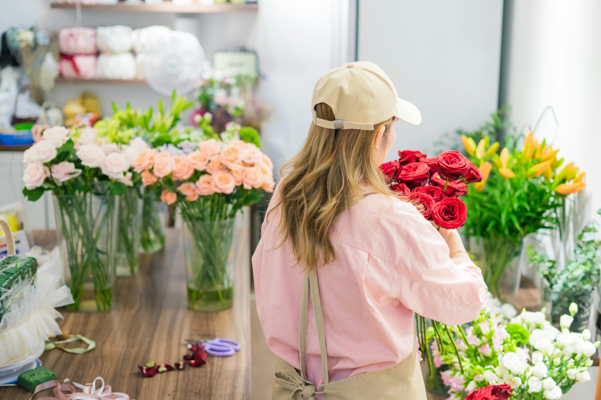 Photo d’une femme, de dos, préparant un bouquet dans une boutique de fleurs.