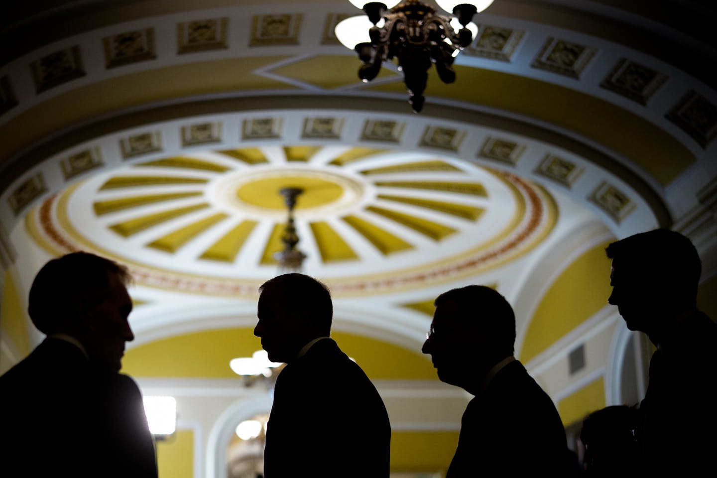 Men in suits shown in shadow underneath elaborate ceiling with arches