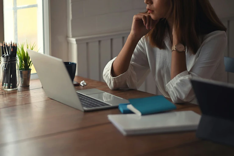A woman sits at a table in front of an open laptop