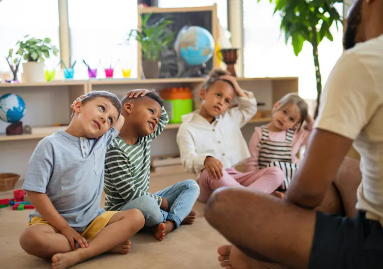 Children seen mirroring the movement of an adult while sitting in a circle.