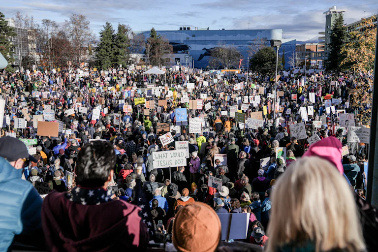 A large crowd gathers on a sunny day in an open area in a city.