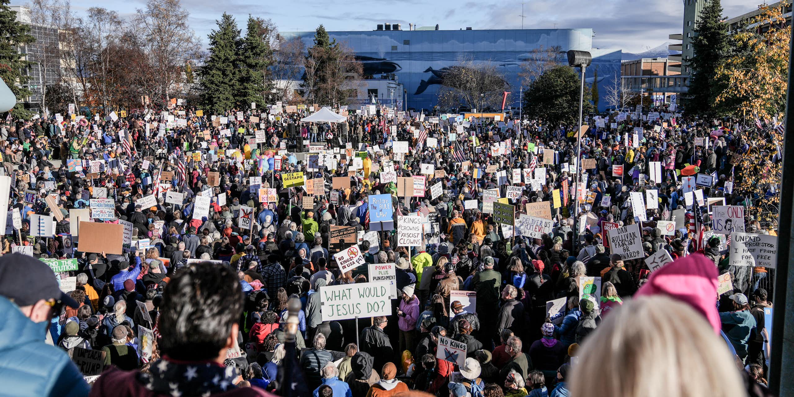 A large crowd gathers on a sunny day in an open area in a city.