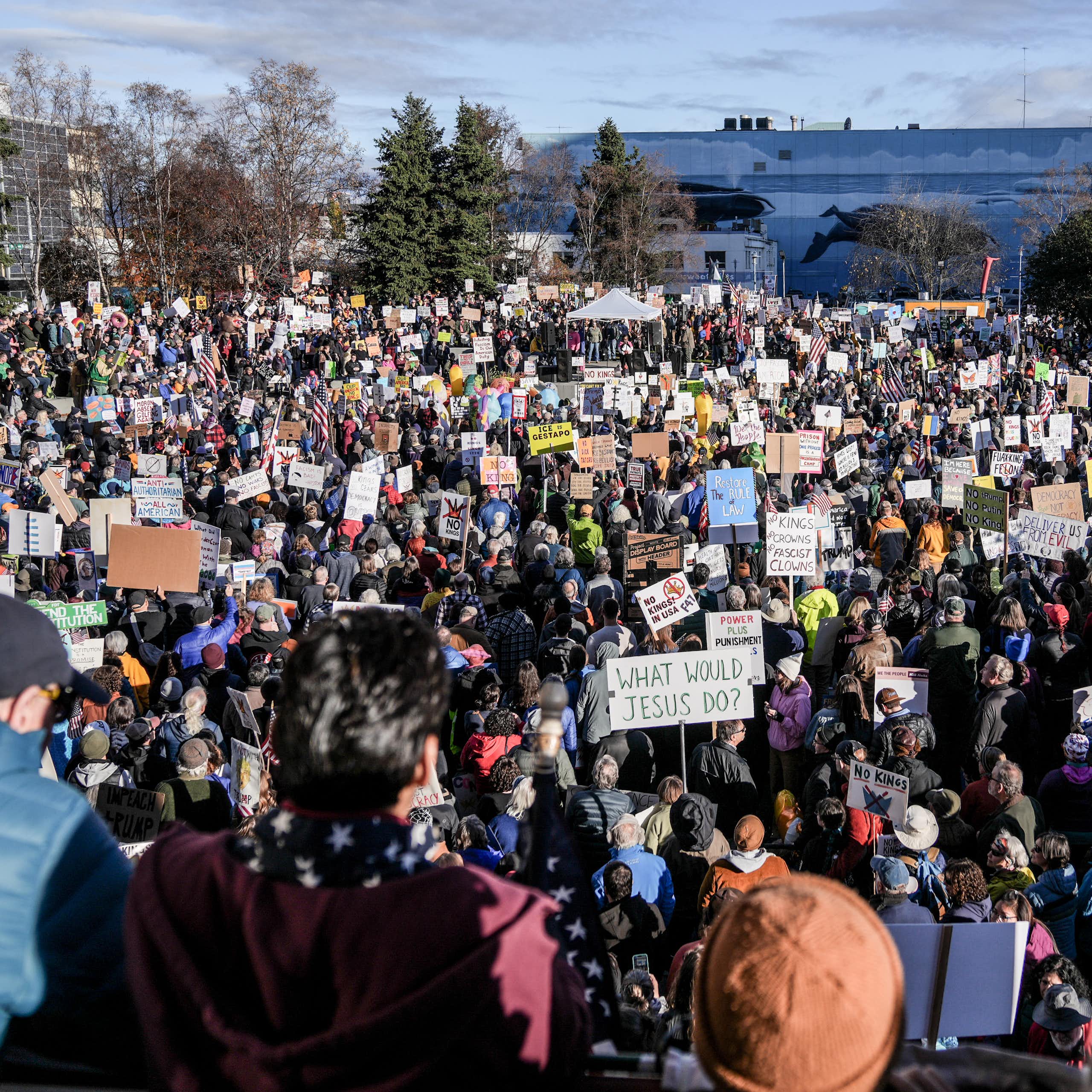 A large crowd gathers on a sunny day in an open area in a city.