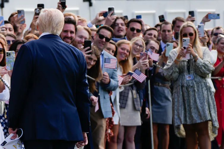 A rotund older man photographed from behind speaks to supporters.