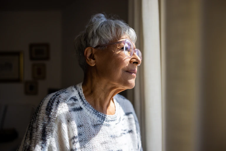 Older woman looks out the window of her aged care facility