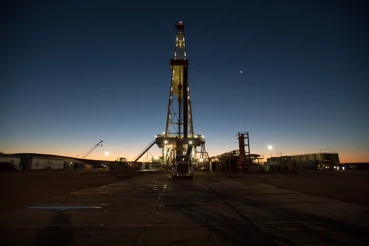 a fracking rig seen at dusk, tall tower and evening sky.