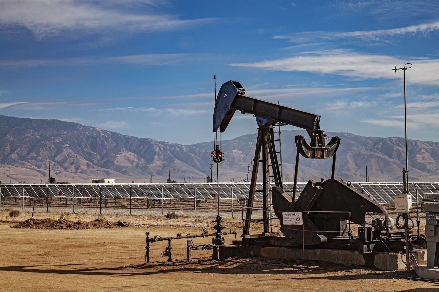 oil pump in foreground and solar panels in background, with mountains at rear.