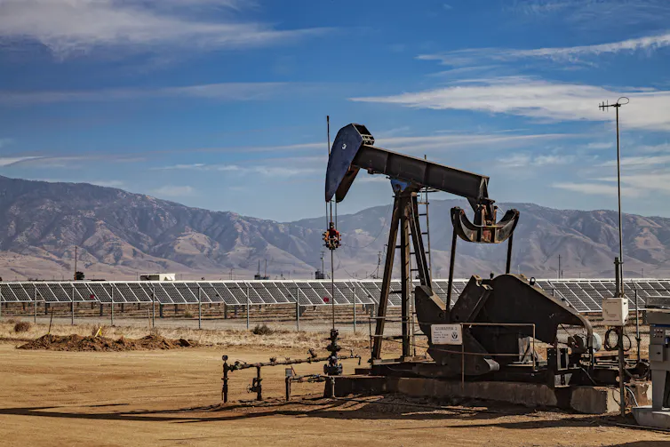 oil pump in foreground and solar panels in background, with mountains at rear.