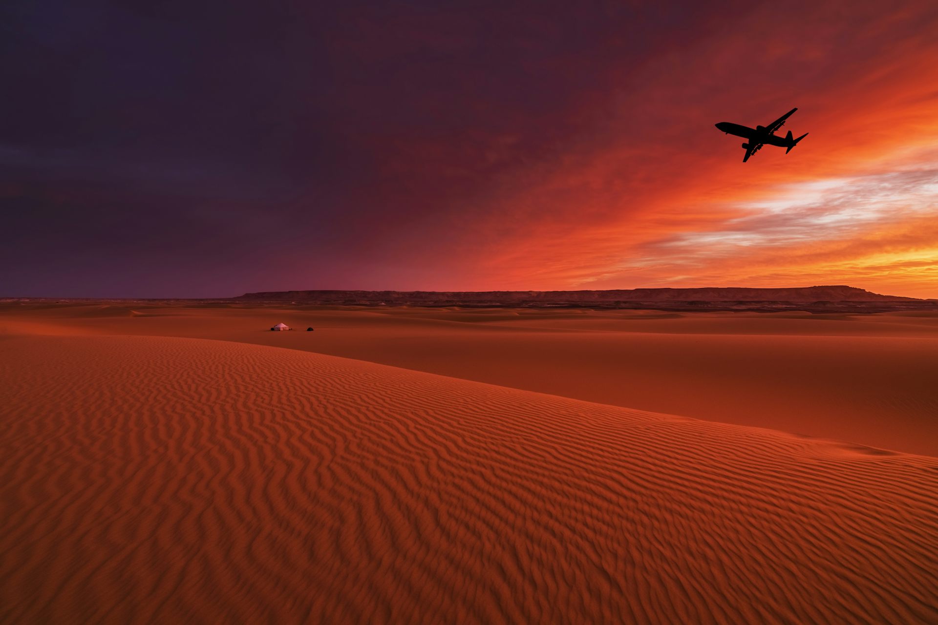 A large plane flies over a desert in the sunset with gold and pink sky in the background