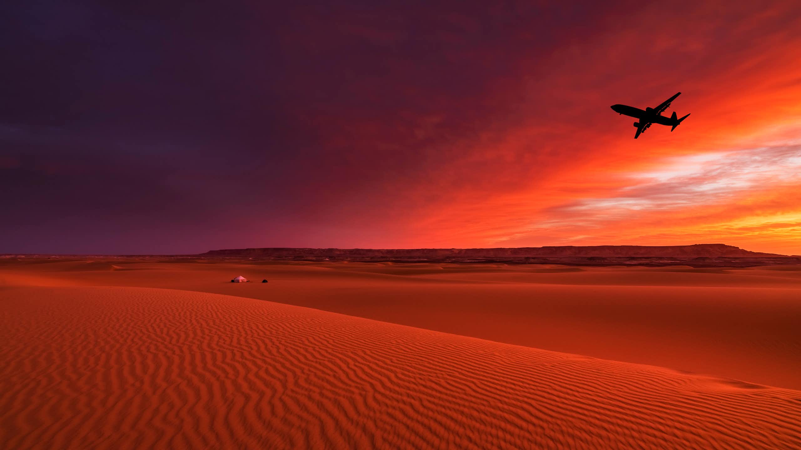 A large plane flies over a desert in the sunset with gold and pink sky in the background
