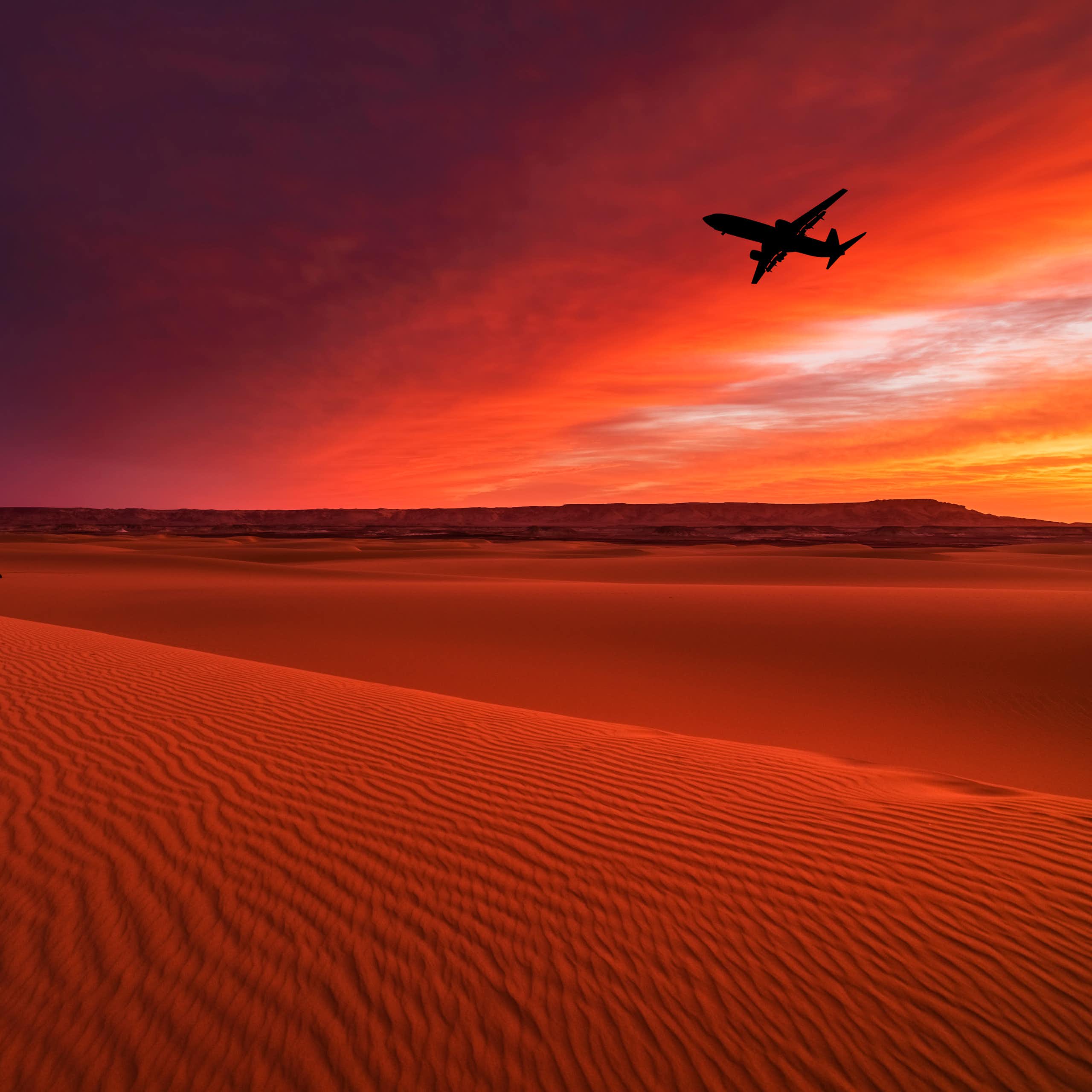 A large plane flies over a desert in the sunset with gold and pink sky in the background