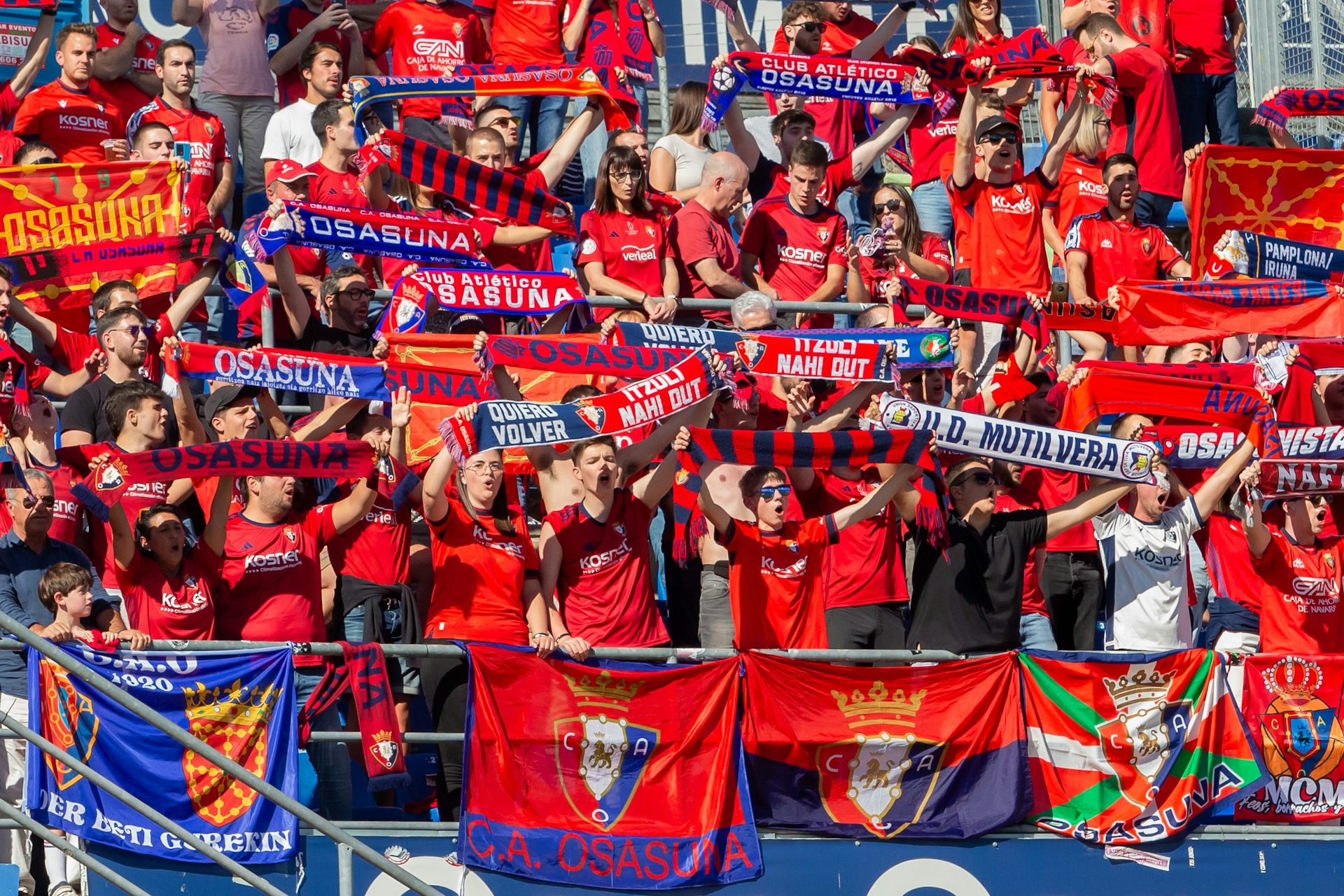 Aficionados vestidos de rojo enseñando bufandas en un estadio.