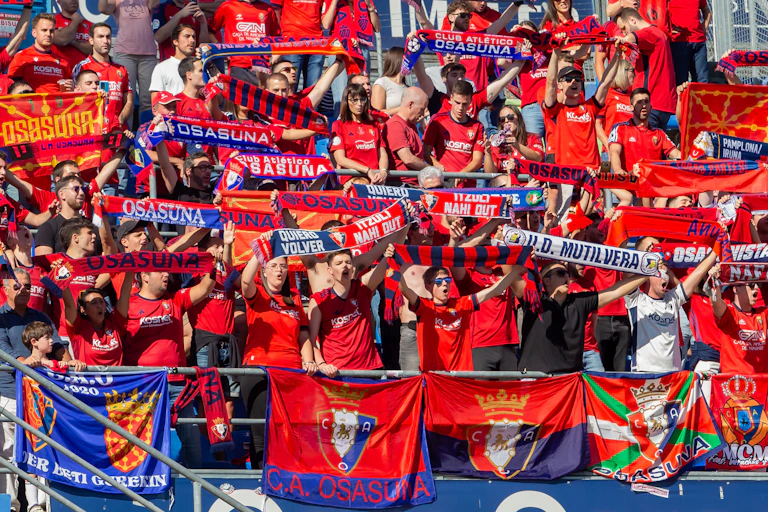 Aficionados vestidos de rojo enseñando bufandas en un estadio.