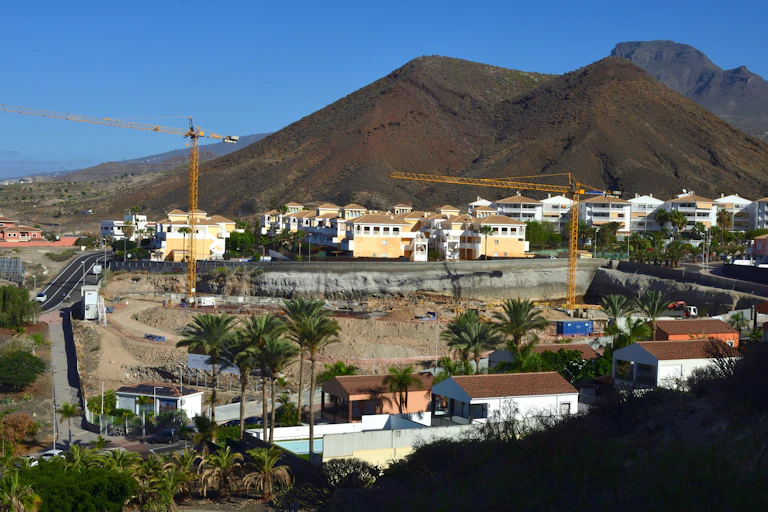 Viviendas en construcción con grúas en un paisaje volcánico.
